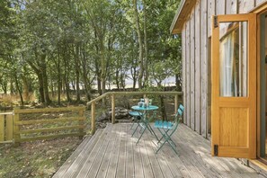 Une terrasse en bois avec une table et des chaises, entourée d’arbres.