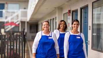 Three individuals in blue aprons walking outside a building with a staircase and a red umbrella in the background.