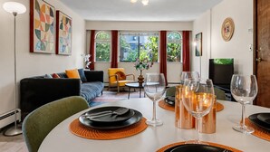 Ein modernes Wohnzimmer mit Essbereich, ausgestattet mit einer Couch, Sesseln, einem für das Essen gedeckten Tisch und Kunstwerken an den Wänden.
