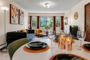 Uma sala de estar moderna com área de jantar, apresentando um sofá, cadeiras, uma mesa posta e obras de arte nas paredes.
