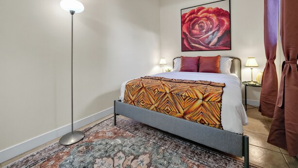 Ein Hotelzimmer mit einem Bett, einer Stehlampe, einem Teppich, einem Rosenbild und Vorhängen.