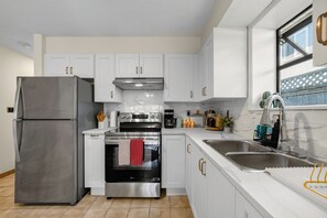 Cozinha moderna com armários brancos, eletrodomésticos de aço inoxidável e janela com vista.