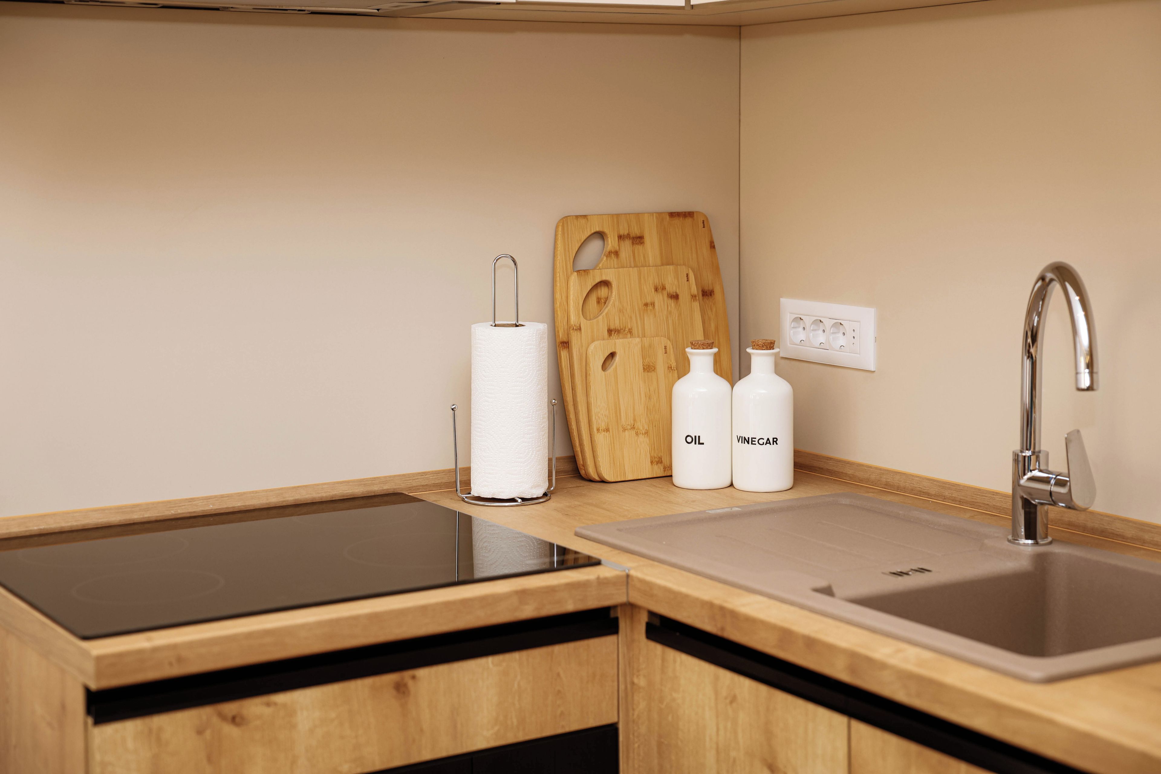 A kitchen with a wooden countertop, a sink, a cutting board, a paper towel holder, and two bottles labeled 'OIL' and 'VINEGAR'.