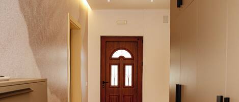 A hallway with a wooden door at the end, recessed ceiling lights, and a wall-mounted light fixture.