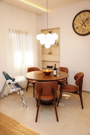 Un coin repas avec une table ronde, des chaises, une bouteille de vin et une horloge au mur.