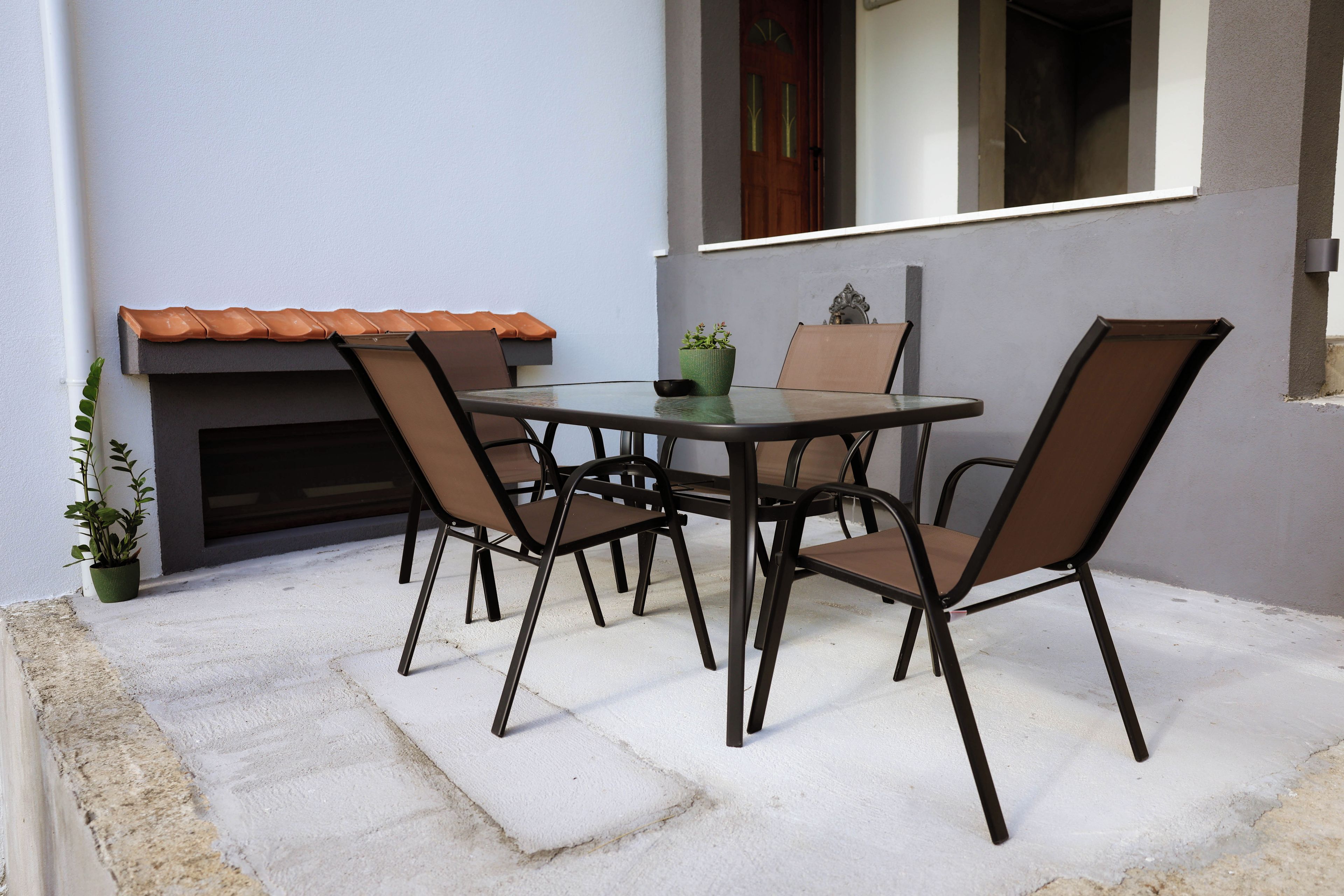 An outdoor patio with a table and chairs, a potted plant, and a tiled roof.