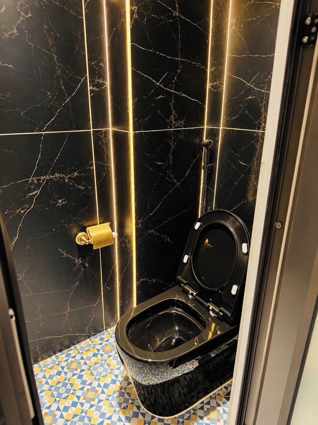A bathroom with a black toilet, marble walls, and a patterned floor.