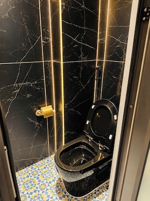 A bathroom with a black toilet, marble walls, and a patterned floor.