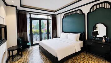 Habitación de hotel con una cama grande, un escritorio, una silla, un televisor y un balcón con cortinas.