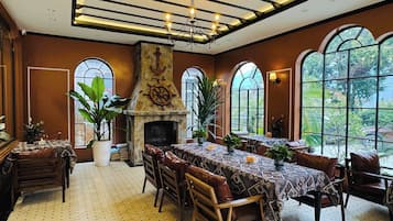 Un comedor con chimenea, ventanas amplias y techo con vigas a la vista.