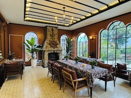 Un comedor con chimenea, ventanas amplias y techo con vigas a la vista.