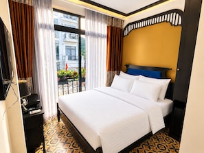 Habitación de hotel con cama, escritorio con teléfono y vista a un balcón con plantas y una bandera.