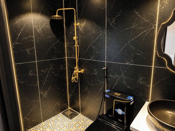 A bathroom with a black marble wall, a gold showerhead, and a black sink.