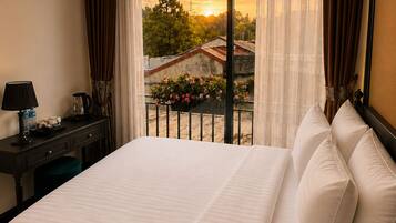 Habitación de hotel con una cama grande, un escritorio con lámpara y vistas a un atardecer desde la ventana.
