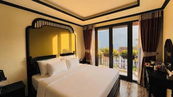Habitación de hotel con una cama grande, una mesita de noche, un aparador y un balcón con cortinas.