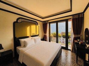 A hotel room with a large bed, a nightstand, a dresser, and a balcony with curtains.