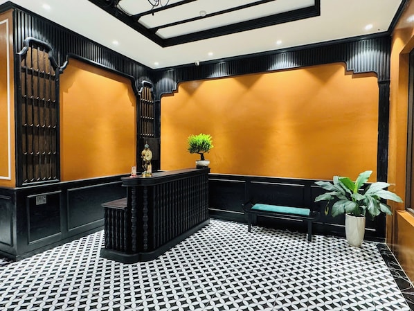 A reception area with a black and white patterned floor, a reception desk, a clock, and a potted plant.