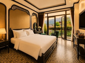 Habitación de hotel con una cama grande, un escritorio con televisor de pantalla plana y un balcón con vistas a zonas verdes y montañas.