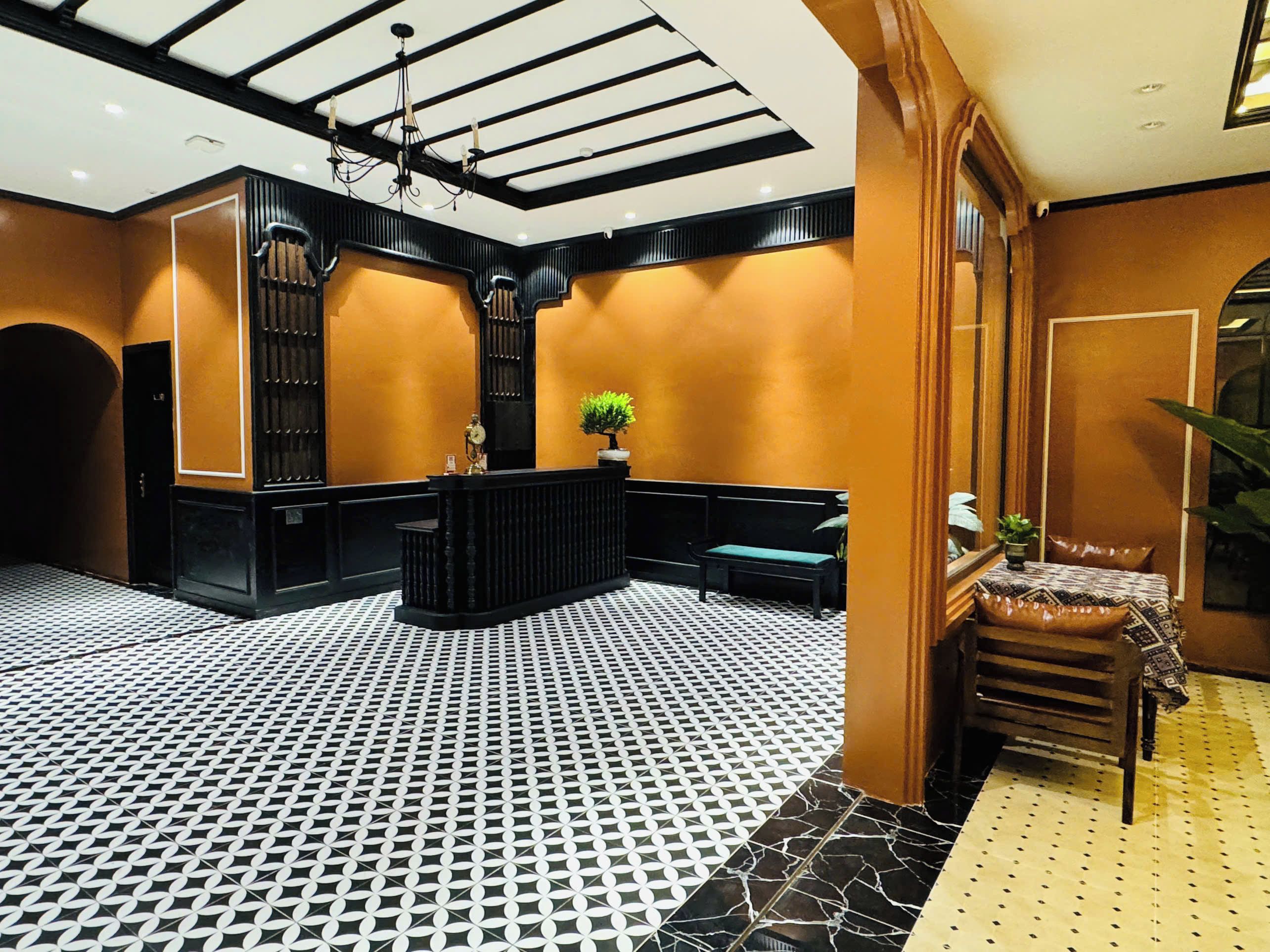 Un hall d’entrée avec un sol à carreaux, un comptoir d’accueil, un espace salon et un grand miroir.