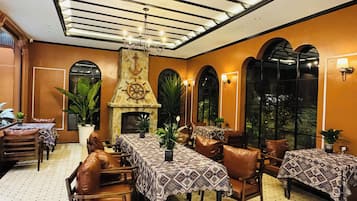 Un comedor con chimenea, sillas de cuero y mesas cubiertas con manteles estampados.