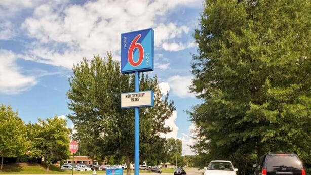 Placa de motel com logotipo '6', uma placa de pare e um estacionamento com carros.