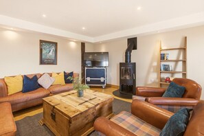 A cozy living room with a sofa set, a wooden coffee table, a fireplace, a television, and a bookshelf. - Drum Barn Roses Bower - North East Escapes (Great Whittington)