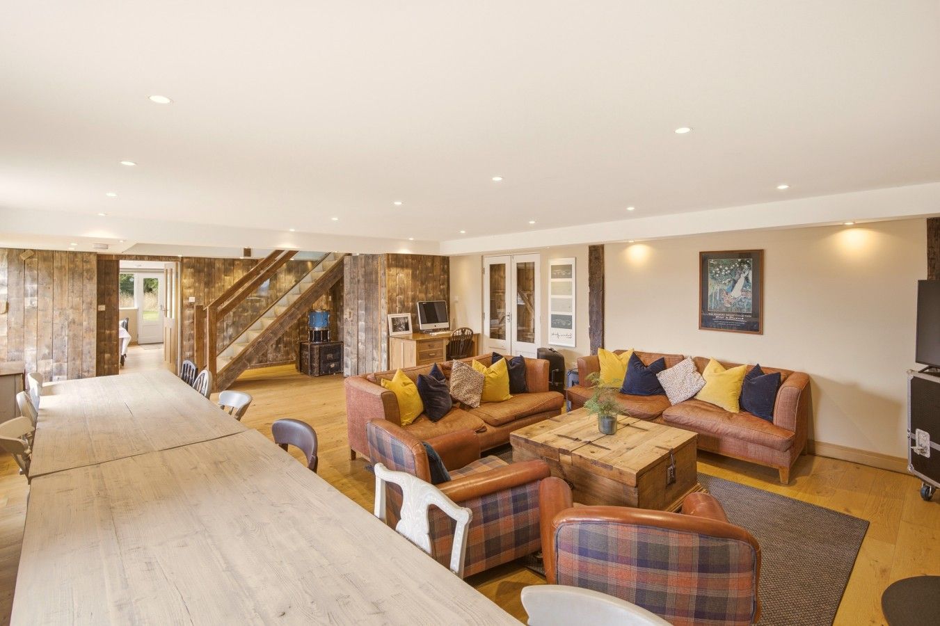 A spacious living area with a wooden dining table, a sofa set, and a staircase leading to an upper floor.