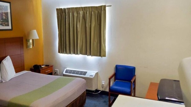 A hotel room with a bed, an air conditioner, a desk, a chair, and a window with curtains. - 1 Queen Bed | Smoking, Kitchen (Richmond VA)