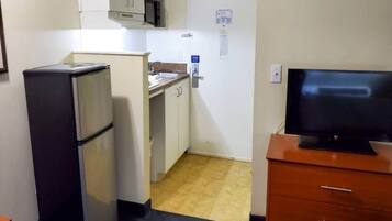 Cocina compacta con refrigerador, microondas, pileta y televisor sobre un mueble de madera.
