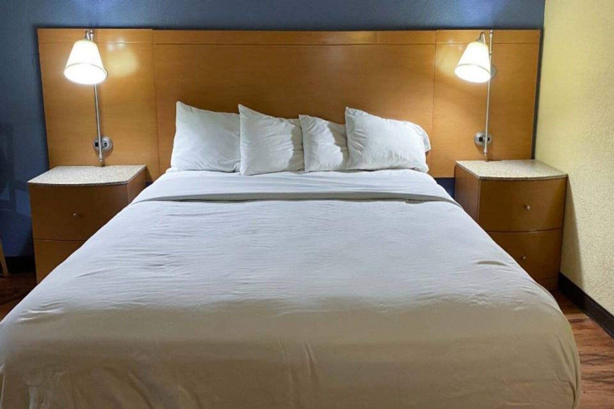 A hotel room with a large bed, two bedside tables, and two wall-mounted lamps.