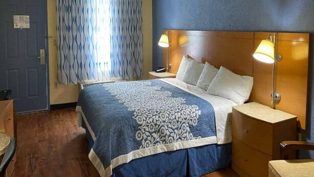 A hotel room with a bed, bedside lamps, a wooden headboard, a nightstand, and a window with curtains. - Spacious Queen Bed Room|Free Wifi (Savannah GA)