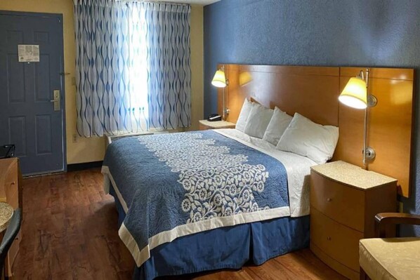 Ein Hotelzimmer mit einem Bett, Nachttischlampen, einem hölzernen Kopfteil, einem Beistelltisch und einem Fenster mit Vorhängen.