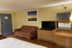 Une chambre d’hôtel avec un lit, un canapé, une télévision, une commode et un tableau au mur.