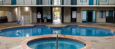 An indoor swimming pool with a hot tub in the center, surrounded by a concrete deck.