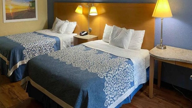 Una habitación de hotel con dos camas, una mesita de noche con un teléfono, una lámpara y un cuadro en la pared.
