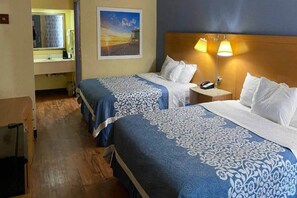 Ett hotellrum med två sängar, ett nattduksbord, en lampa, en tavla på väggen och ett badrum som syns i bakgrunden.