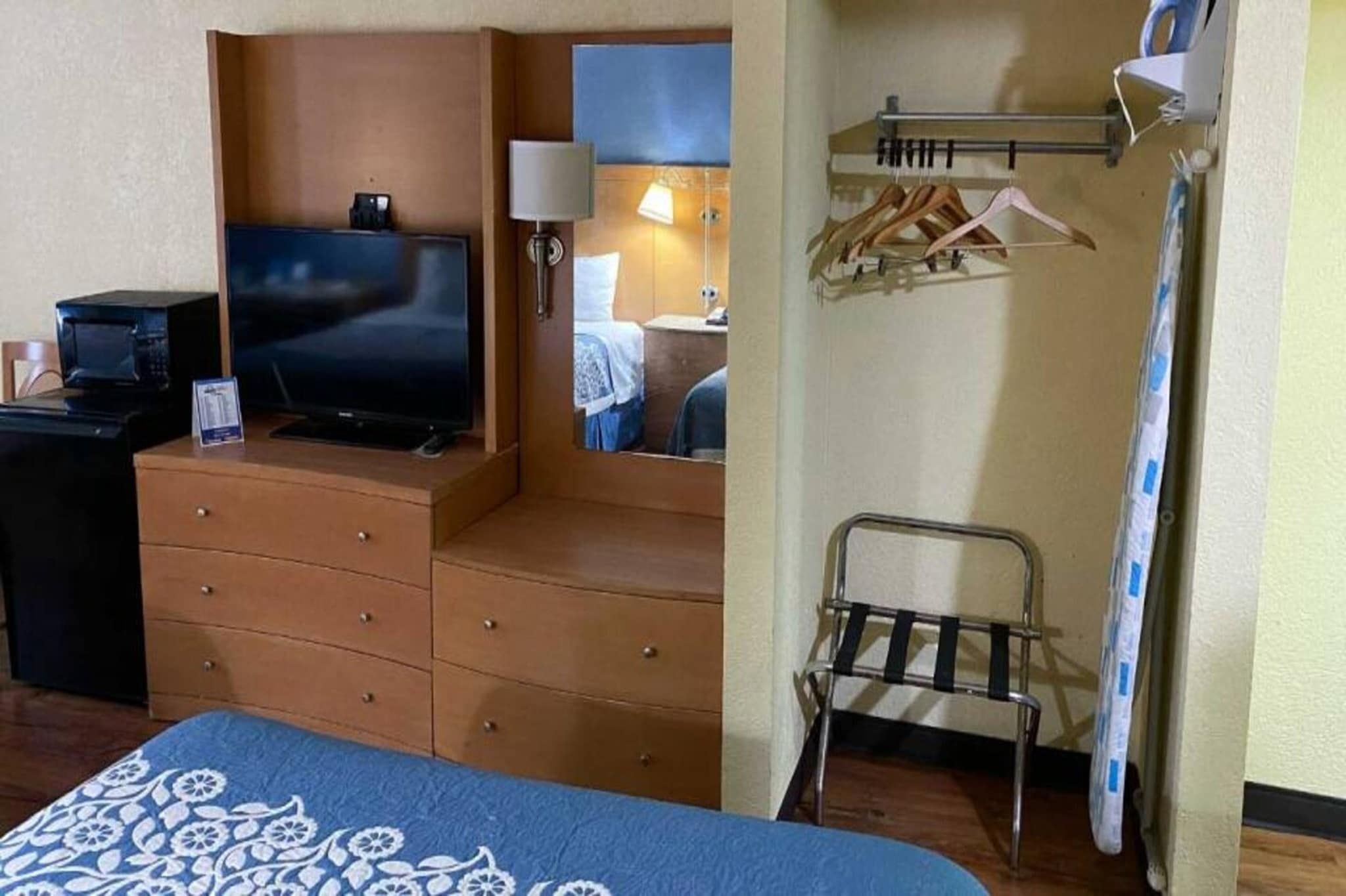 Een hotelkamer met een bed, een dressoir, een televisie, een spiegel, een lamp, een kapstok en een douche.