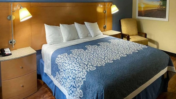 A hotel room with a large bed, two bedside lamps, a chair, a desk with a phone, and a framed picture on the wall. - Cozy 2-Bed Queen|Pool|Free Wifi (Savannah GA)