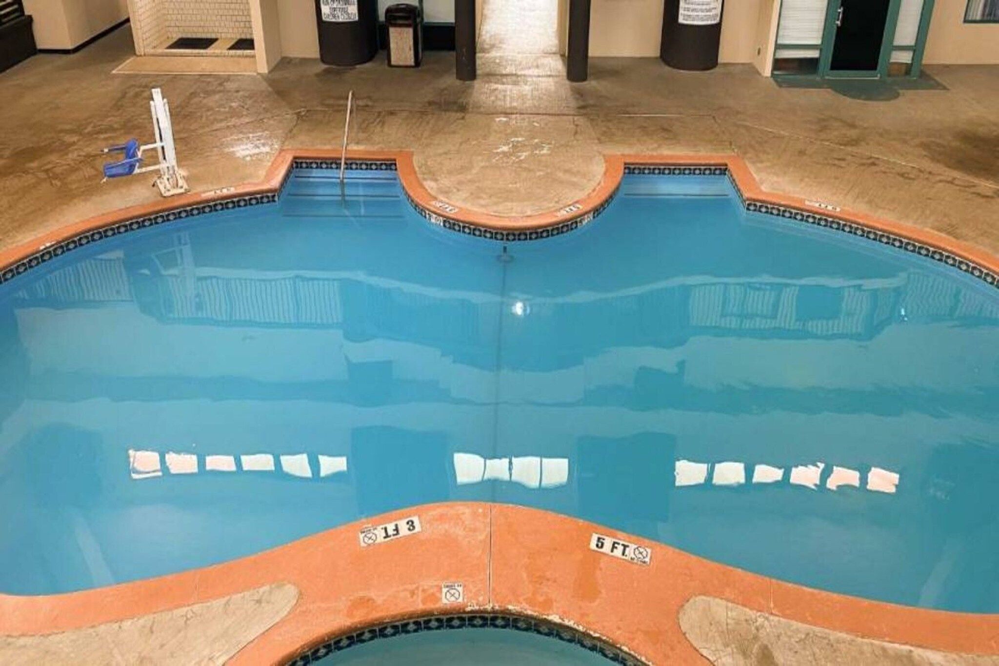 A swimming pool with a blue interior and an orange border, surrounded by a concrete deck.