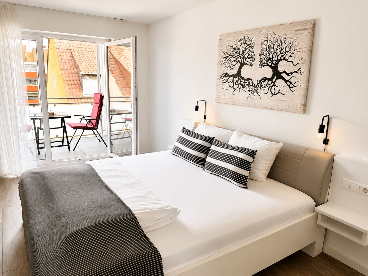 A hotel room with a bed, a view of the outside balcony, and a painting on the wall.