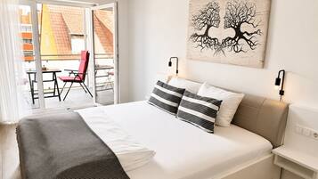 A hotel room with a bed, a view of the outside balcony, and a painting on the wall.
