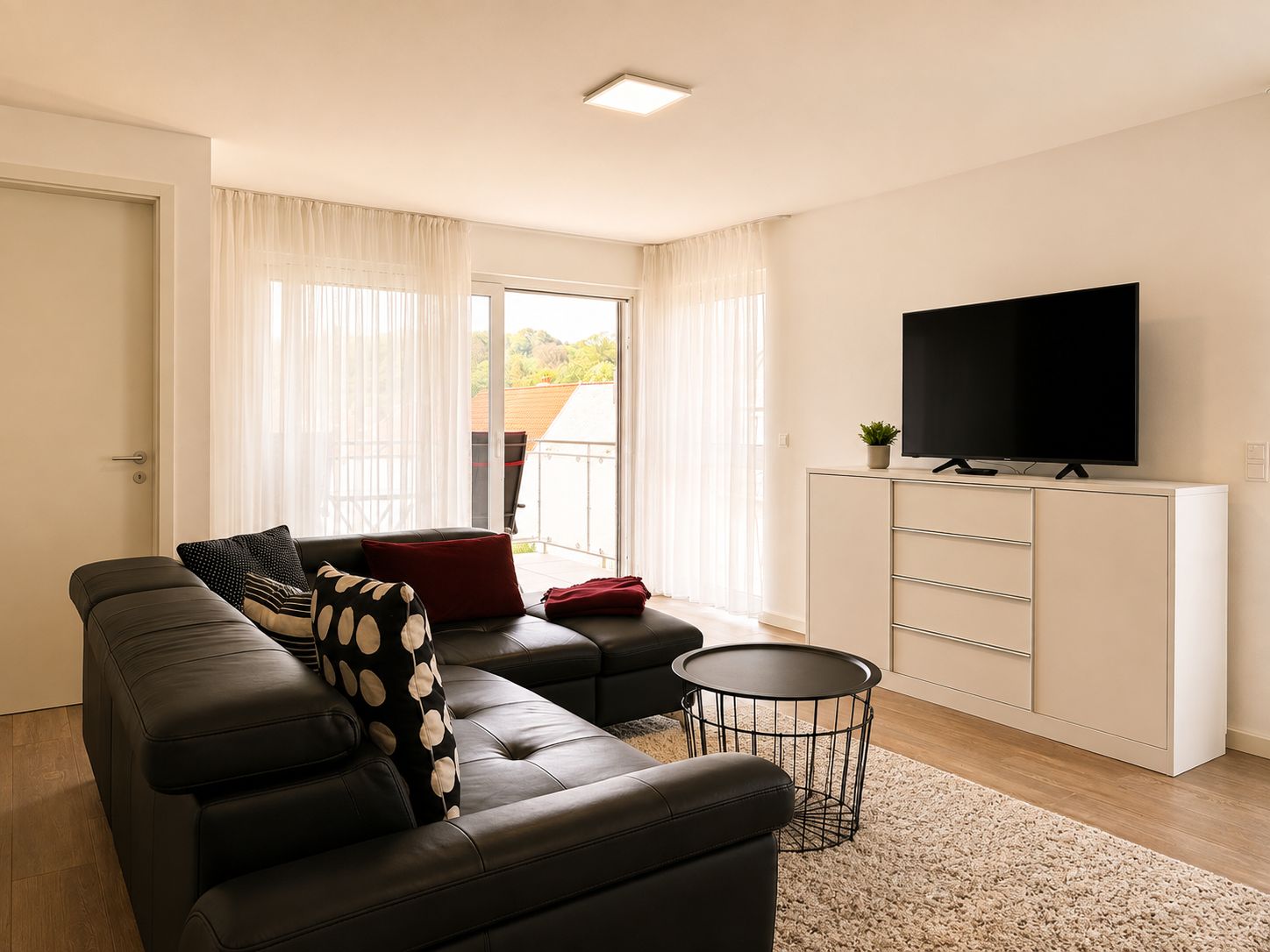 Un salon moderne avec un canapé en cuir, un téléviseur à écran plat posé sur un meuble et un balcon agrémenté de rideaux.