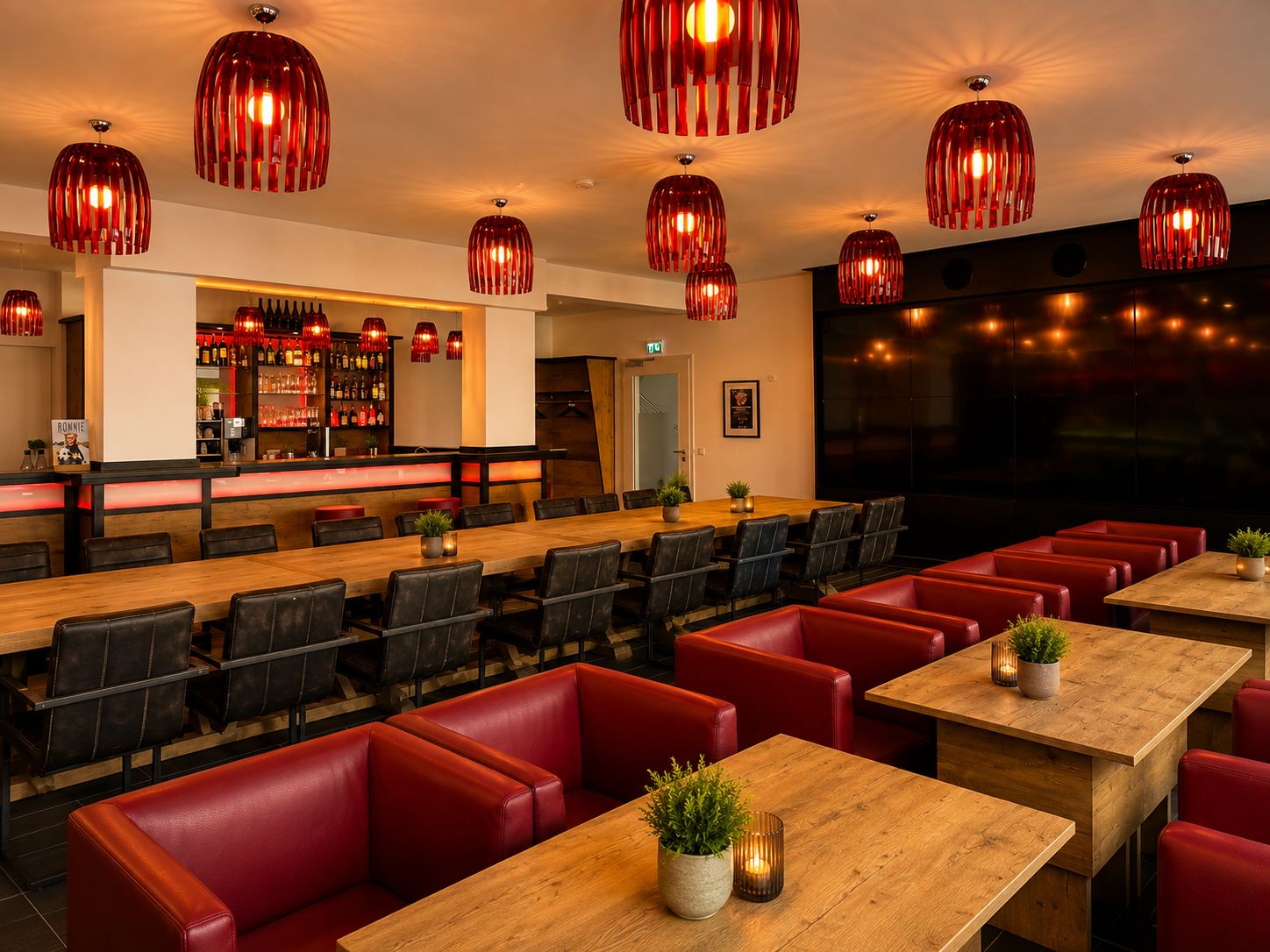 A restaurant with multiple dining tables and booths, a bar area, and red pendant lighting.