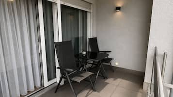 Ein Balkon mit Glastisch und zwei Stühlen, eine Schiebetür aus Glas und einer strukturierten Wand.