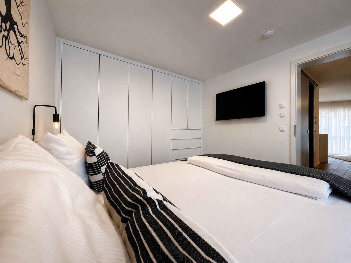 A modern bedroom with a bed, a wardrobe, a flat-screen TV, and a bedside lamp.