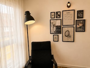 A room with a black chair, a floor lamp, and various framed pictures on the wall.