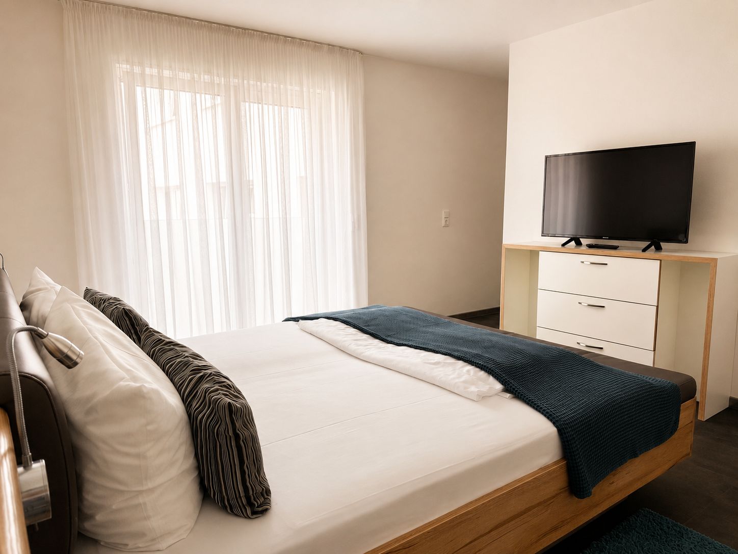 A hotel room with a bed, a television on a stand, a bedside table, and a window with curtains.