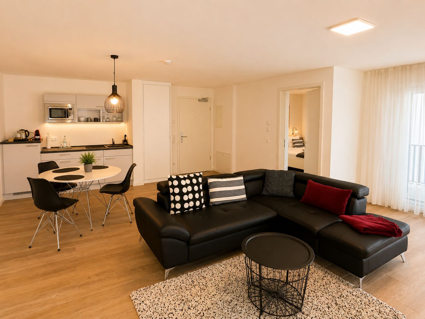 A modern living room with a black sectional sofa, a round coffee table, and a dining area with a white table and black chairs.