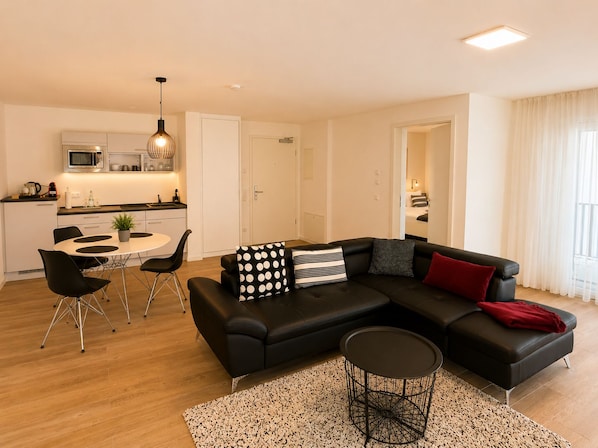 A modern living room with a black sectional sofa, a round coffee table, and a dining area with a white table and black chairs.