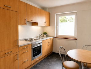 A modern kitchen with wooden cabinets, a built-in oven, a sink, and a window providing natural light.